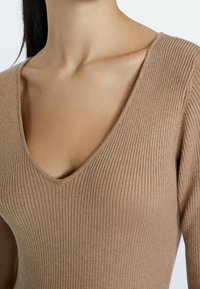 Top a V con costo rib di colore marrone chiaro, caratterizzato da maniche lunghe e una silhouette aderente, realizzato in un tessuto morbido e strutturato.