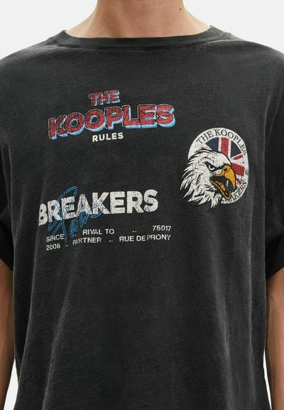 Juodas grafikos marškinėliai, pagaminti iš minkštos medvilnės, su spalvingu tekstu, erelio emblema ir įvairiais spausdintais detalėmis kontrastinga balta ir mėlyna spalva.