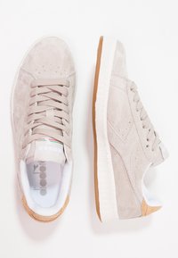 Jasnoszare zamszowe sneakersy z białą środkową podeszwą i gumową, brązową podeszwą zewnętrzną. Mają wyściełany kołnierz i logo na języku.