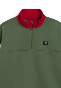Pull vert forêt à demi-fermeture éclair avec col montant rouge et petit écusson du logo Vans noir sur la poitrine.