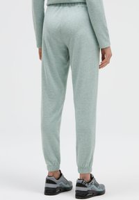 Hellgrüne, weiche Jogginghosen aus Stoff mit elastischem Bund und Bündchen an den Knöcheln, kombiniert mit schwarzen und grauen Sneakers.