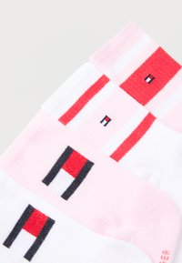 Trois paires de chaussettes basses en blanc et rose avec des rayures rouges et un logo géométrique tricoté en noir, rouge et blanc.