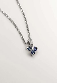 Collar de cadena de plata con un racimo de tres piedras azules redondas y un colgante circular adornado con pequeñas piedras preciosas transparentes.