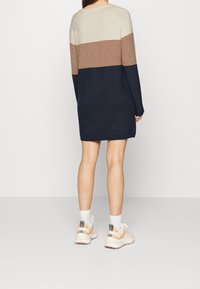 Abito a maglia caratterizzato da blocchi di colore orizzontali: crema, beige e blu navy. Maniche lunghe, colletto rotondo, abbinato a sneakers chiare.