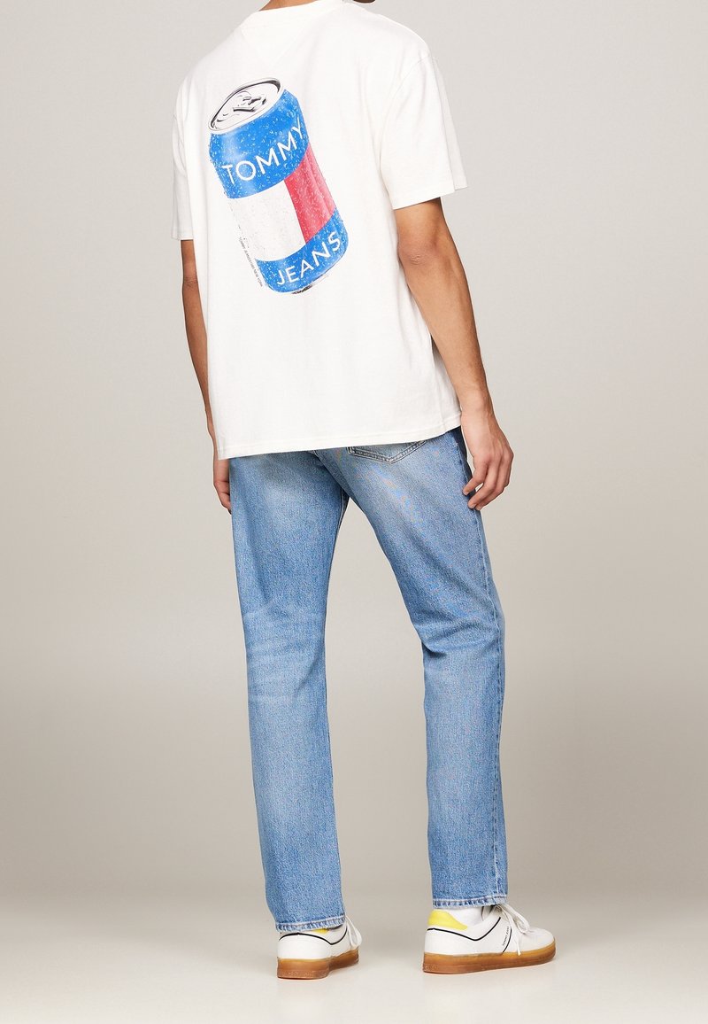 White cotton t-shirt featuring a blue and red can design on the back, paired with light blue straight-leg jeans and white shoes.