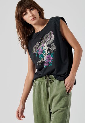 T-shirt sans manches noir avec un imprimé graphique représentant des fleurs et un crâne. Associé à un pantalon de survêtement vert avec cordon de serrage et détails sur les côtés.