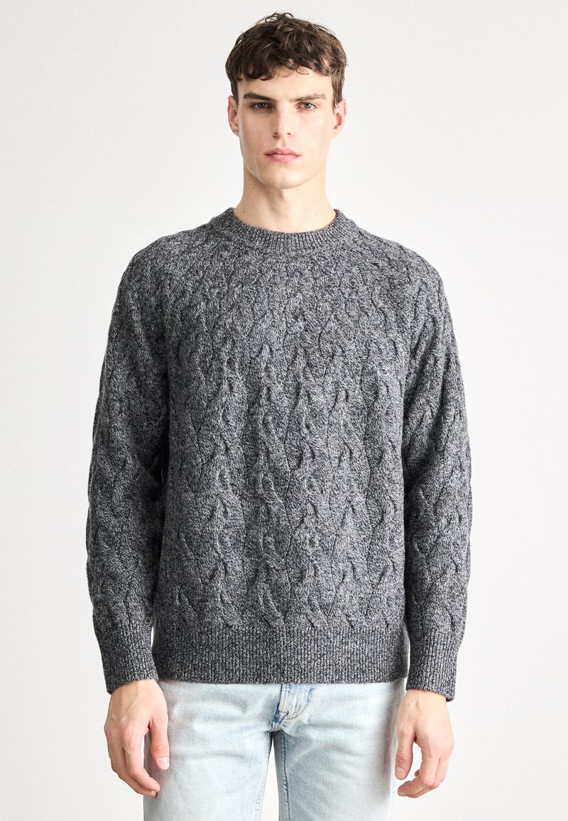 Tumši pelēks džemperis ar apaļu izgriezumu un garām piedurknēm. Bieza tekstūra un ribota apmale. Valkāts virs gaiši zilām džinsu biksēm.