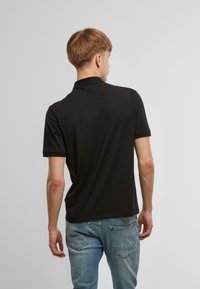 Fekete pólóing gallérral és rövid ujjakkal, minimalista dizájn. Fakó kék farmerrel párosítva, amely karcsú szabású és laza stílusú.