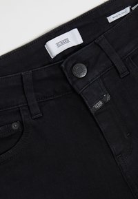 Jeans de mezclilla negra con una textura suave, que cuentan con un cierre de botón, bolsillos cosidos y etiquetas que indican "CLOSED" y "MADE IN ITALY."