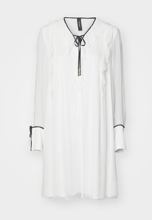 White blouse with ruffled front, long sleeves, and a tie neckline. Features black accents at sleeve cuffs and gently pleated texture.