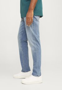 Light blue denim jeans with a straight cut, faded texture, and minimal stitching details. Paired with white sneakers.