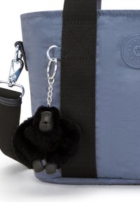 Borsa a mano di tessuto blu con un portachiavi a forma di gorilla peloso nero attaccato con una clip argentata, completata da una tracolla nera e dettagli del logo.