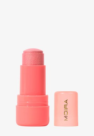 Bâton de maquillage rose corail à texture pailletée, à côté d'un capuchon assorti marqué "MOIRA" en lettres dorées sur fond blanc.