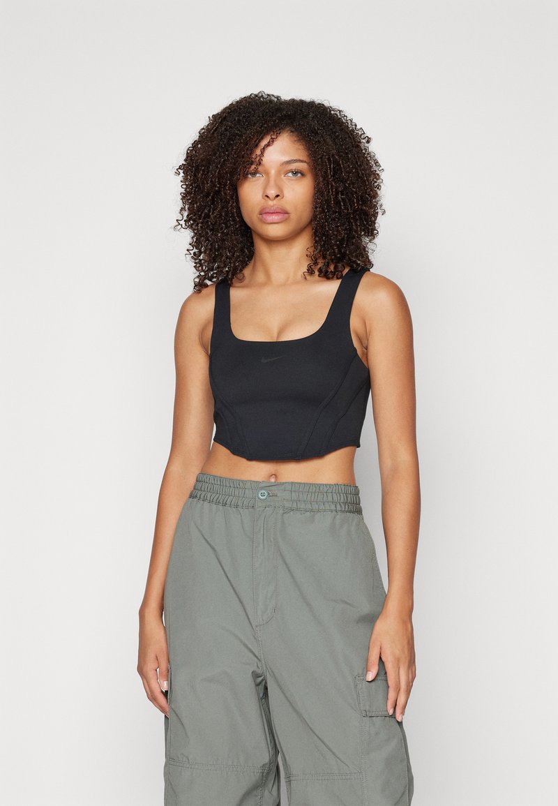 Brasile sportivo nero con spalline larghe, scollatura quadrata e design aderente. Abbinato a pantaloni cargo grigi chiari a vestibilità ampia con vita elasticizzata.