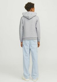 Felpa grigia in cotone con cappuccio, polsini a coste e tasca a marsupio frontale. Abbinata a jeans a taglio rilassato di colore blu chiaro e sneakers bianche.