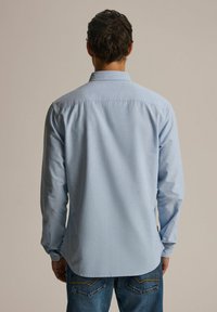 Jasnoniebieska koszula z długim rękawem i kołnierzykiem zapinanym na guziki, wykonana z teksturowanej tkaniny, o zaokrąglonym dole, w połączeniu z dżinsami.
