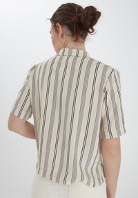 Camicia a maniche corte beige con righe nere verticali, dotata di colletto e vestibilità rilassata. Tessuto morbido, dettaglio sulla cucitura posteriore.