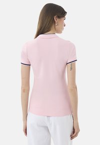 Polo rosa con design aderente, maniche corte e rifiniture blu navy al colletto e ai bordi delle maniche. Texture liscia.