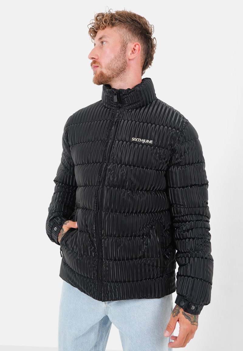 Zwarte pufferjack met een gestikte textuur, hoge kraag, ritssluiting en zijzakken. Gemaakt van glanzend materiaal met detail van het merklogo.