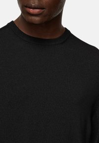 Black knitted sweater with a ribbed texture and a classic crew neckline, featuring smooth fabric and a fitted look.