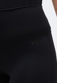 Κοντινή λήψη μαύρων κολαν με ψηλή μέση και διακριτικό λογότυπο «BORG» τυπωμένο στο πλάι κοντά στο ισχίο.