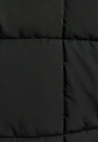 Gros plan sur un tissu matelassé noir avec des coutures horizontales et verticales formant des carrés rembourrés.