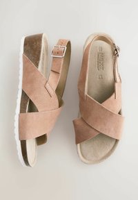 Sandales en suède tan avec des sangles croisées, une boucle ajustable et une semelle texturée légère, présentant un léger design compensé. Doublure intérieure douce.