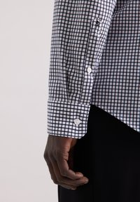 Wit button-up shirt met een marineblauw ruitpatroon. Heeft lange mouwen en cuffs met witte knopen. Gladde stofstructuur.