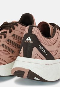 Baskets Adidas Adizero en rose poussiéreux et marron, avec une tige en maille, une épaisse semelle blanche avec SwirlFoam et des accents de marque distinctifs.