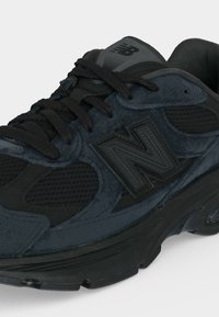 Sneaker New Balance bleu marine foncé et noir avec empiècements en daim et mesh, semelle épaisse, lacets noirs et logo "N" marqué sur le côté.