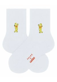 Weiße Baumwollsocken mit einem gestickten gelben Bärenmotiv und roten Akzenten, auf der Sohle steht der Text "FALKE x HARIBO".