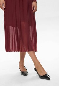 Rochie plisată burgundy cu textură cu buline, asortată cu pantofi slingback cu vârf ascuțit negri. Material neted și siluetă elegantă.