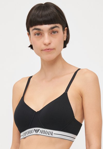 Black wireless bra made of smooth fabric, featuring a triangular design, adjustable straps, and a white branded elastic band.
