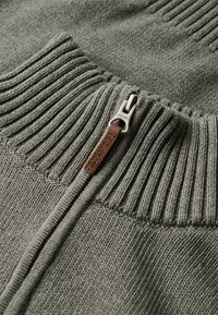 Grauer Strickpullover mit einem gerippten Kragen und einem Reißverschluss mit einem Lederzipper. Weiche Textur mit einem dezenten Strickmuster.