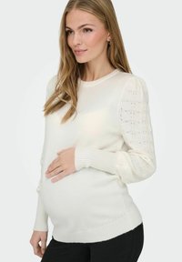 Biały sweter ciążowy z dzianiny, z ribbowymi mankietami i teksturowanym, wzorzystym wzorem na rękawach. Miękki, elastyczny materiał gwarantujący komfort.