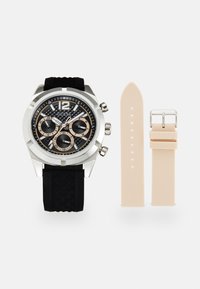 Reloj con correa de goma negra y caja plateada, esfera negra texturizada y subesferas de cronógrafo beige. Incluye una correa adicional beige.