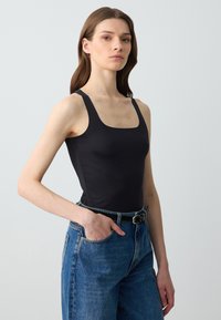 Canotta nera aderente con scollatura quadrata e spalline larghe, abbinata a jeans in denim blu a vita alta.