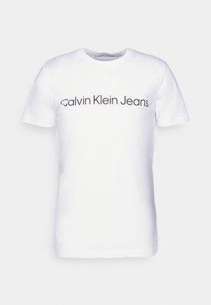 Fehér pamut póló, amelyen a mellkason vastag fekete betűkkel a "Calvin Klein Jeans" felirat található. Klasszikus kerek nyakú és rövid ujjú.