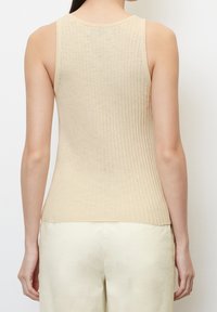 Beige ribbet tank top, uden ærmer, blød tekstur, rund halsudskæring og lige kant. Sat sammen med lyse bukser.