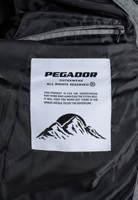 Valge Pegador välisriiete label mustal kangal mägigraafikaga ja tekstiga sooja ja seikluse kohta linna džunglis.