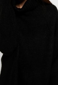 Černý pletený svetr s vysokým žebrovaným rolákem; texturovaná látka; volné dlouhé rukávy; měkký vzhled.