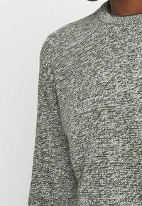 Gestrickter Pullover in Olivgrün und Weiß mit strukturierter Oberfläche, mit Rundhalsausschnitt und langen Ärmeln.
