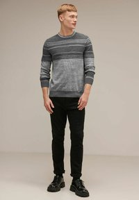 Grårandig tröja med rund halsringning och långa ärmar, kombinerad med svarta slim-fit jeans och svarta snörskor. Platt texturerad yta.