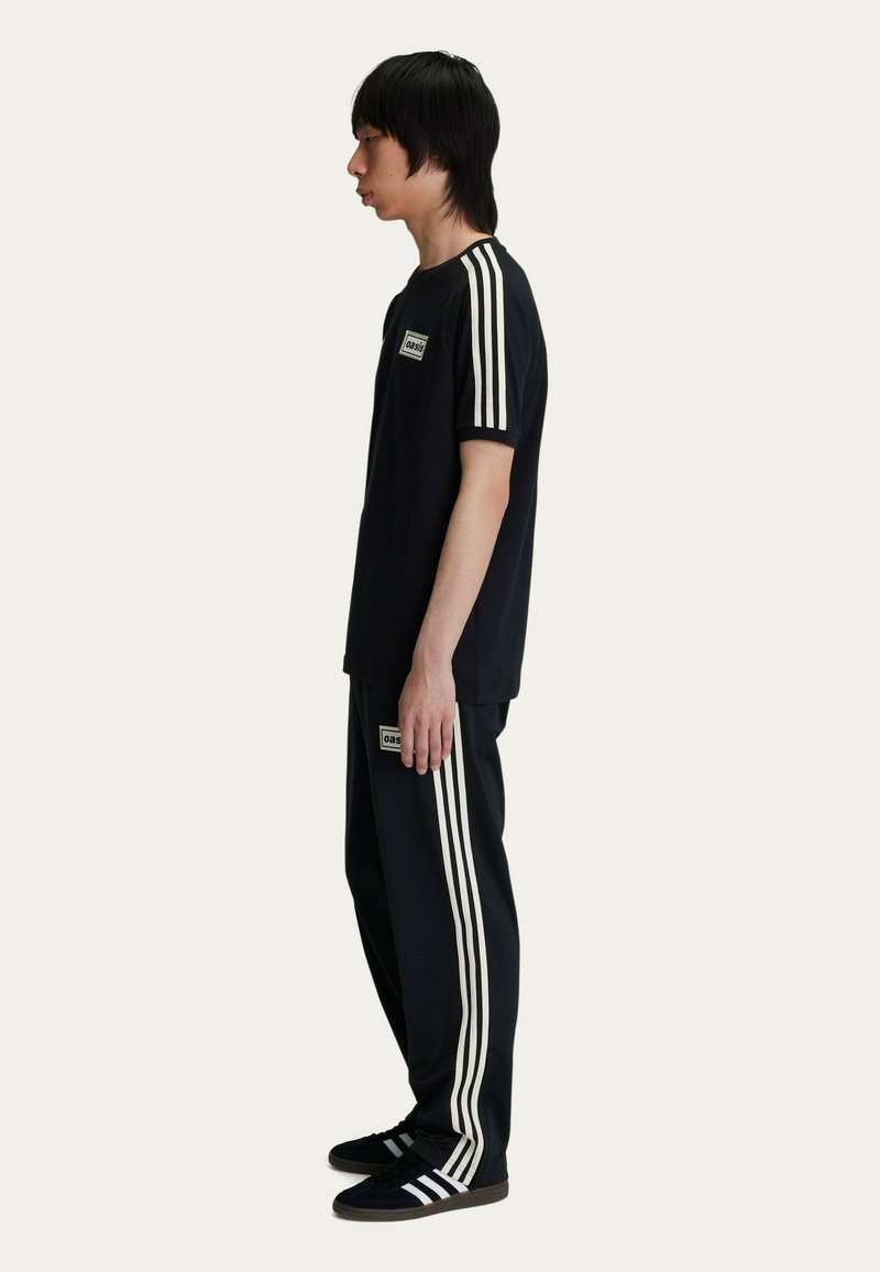 Set di abbigliamento sportivo nero composto da una t-shirt nera con strisce bianche e pantaloni neri coordinati con strisce bianche laterali e dettagli con logo.