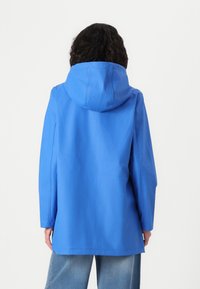 Veste à capuche bleue en matériau lisse et résistant à l'eau. Elle est dotée de manches longues et d'une coupe droite, tombant à mi-cuisse.
