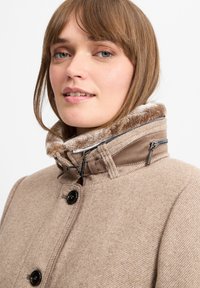 Beige uldblandingsfrakke med høj krave, der har en blød faux fur-foring, lynlåslommer og sorte knapper. Glat tekstur, skræddersyet pasform.