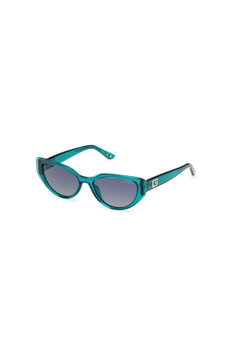Gafas de sol cat-eye turquesas con lentes grises degradados, marco de plástico transparente, grabado sutil del nombre de la marca y un distintivo acento de logo metálico.