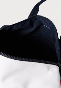 Τσάντα από καμβά με κρεμ εξωτερικό και ναυτικό φερμουάρ. Το εσωτερικό είναι από ναυτικό ύφασμα, με λογότυπο τυπωμένο μέσα. Κλείνει με φερμουάρ στην κορυφή.