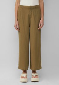 Pantaloni a gamba larga in tessuto verde oliva con una texture liscia, dotati di chiusura a bottone e passanti per cintura, abbinati a sandali con plateau color crema.