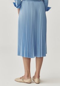 Gonna plissettata azzurro chiaro in tessuto morbido, che arriva sotto il ginocchio. Abbinata a ballerine beige con una cinghia e punta arrotondata.